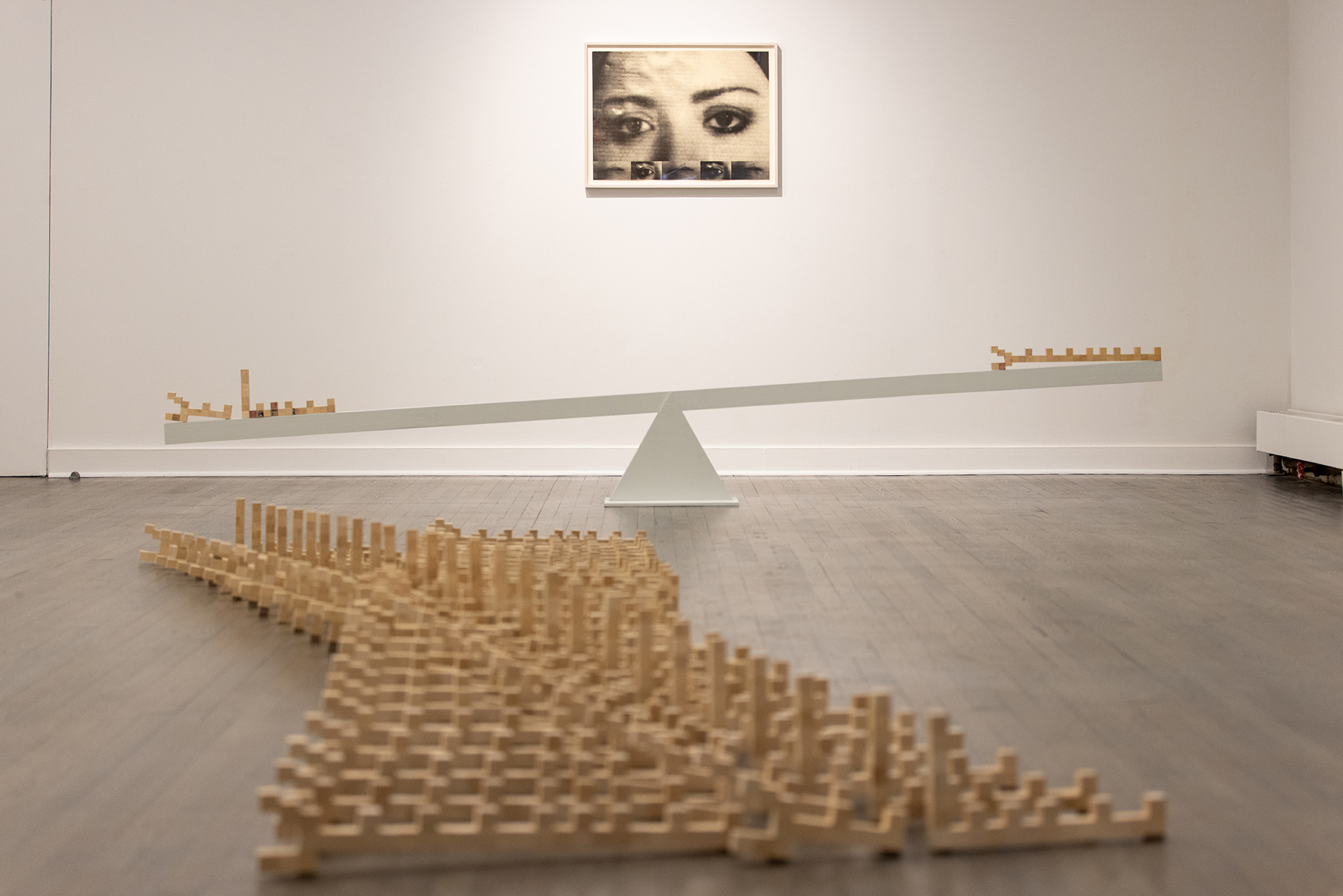 The Arabic words benshinand and benshaanand rendered in wooden blocks sit on either end of a 10' white wooden seesaw. The left word appears slightly heavier.