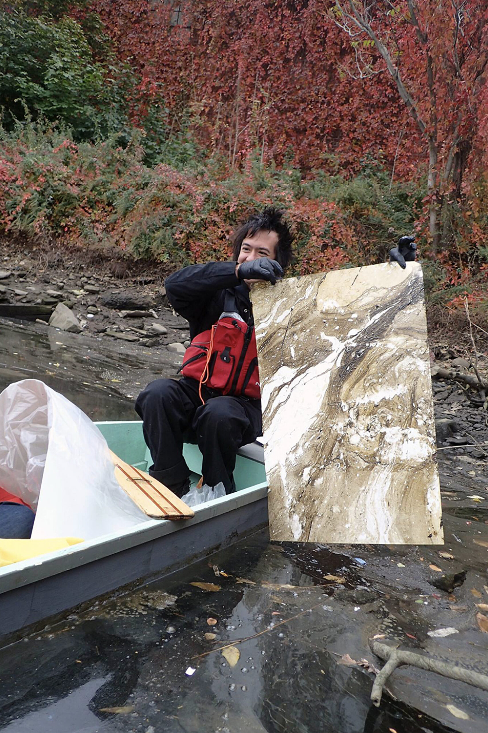 Photo of the artist floating on the Newtown Creek, pulling marbling-like images from pollution and residue on the surface of the creek