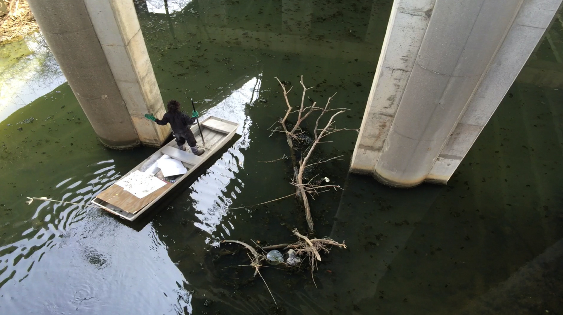 The artist floats on a small boat beneath a bridge on Flushing Creek in Queens, NY