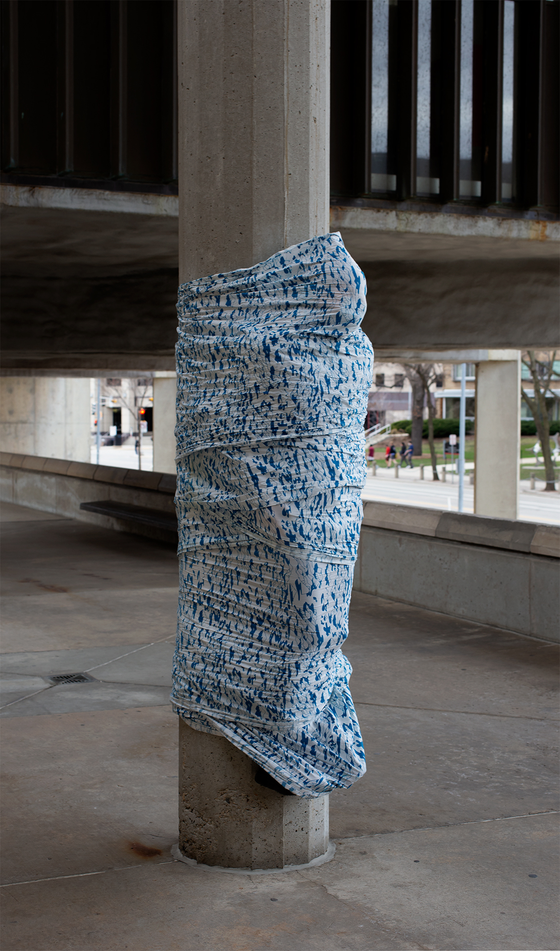 The artist is covered and bound to a column with 20 yards of screenprinted fabric as part of a performance