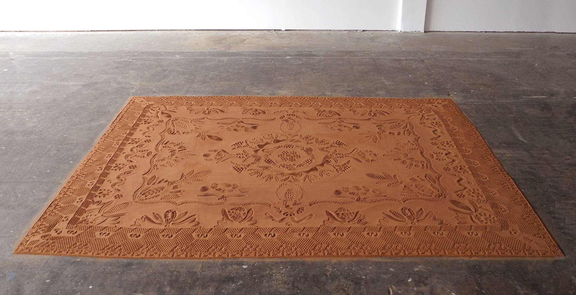 Low relief sculpture mimicking an intricate patterned rug, made with modified shoe soles imprinting ground & sifted Oklahoma red dirt