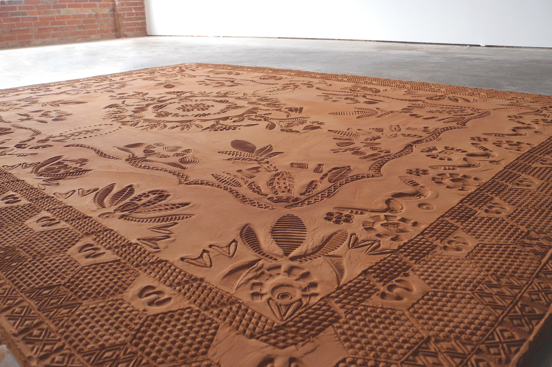 Detail of a low relief sculpture mimicking an intricate patterned rug, made with modified shoe soles imprinting ground & sifted Oklahoma red dirt