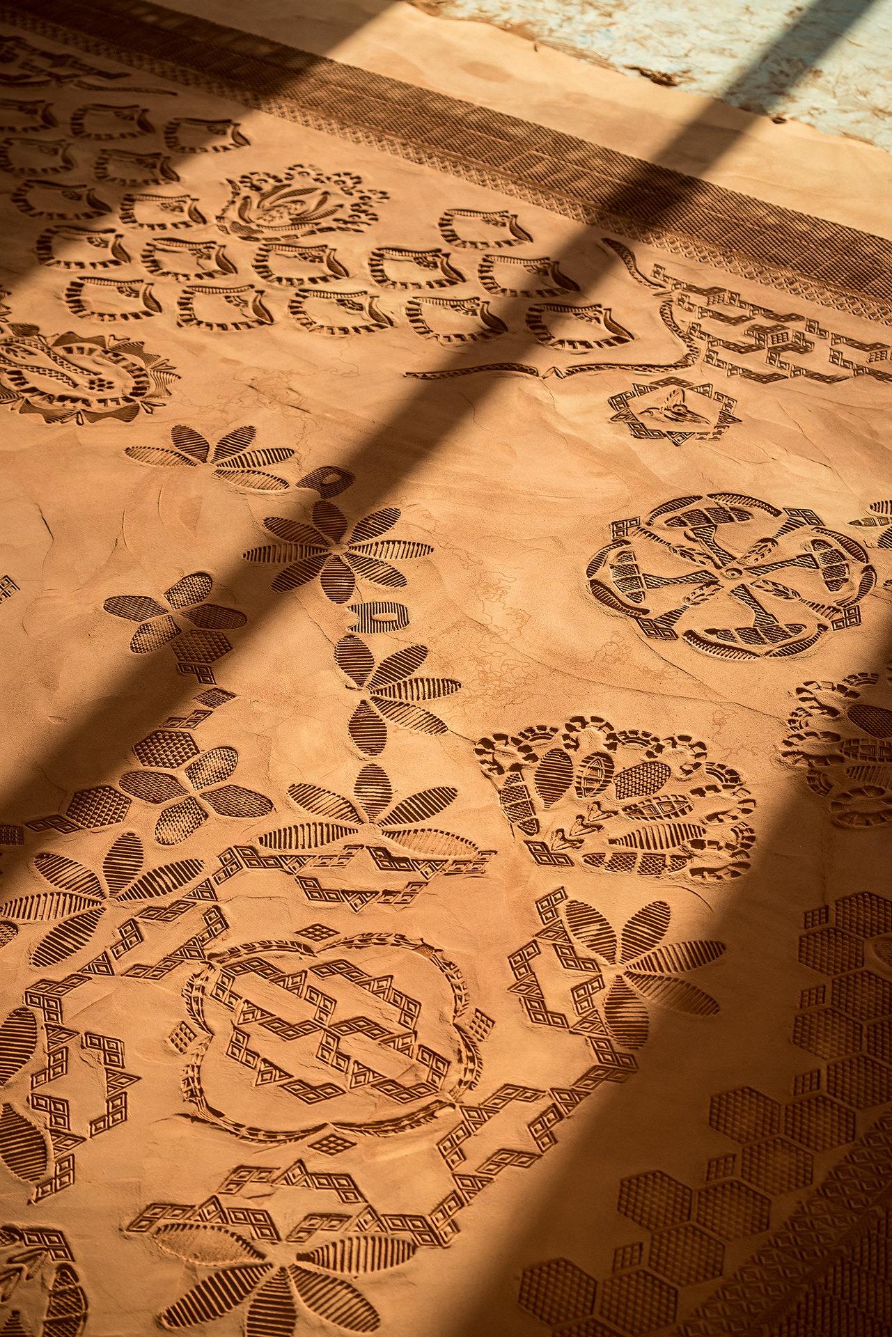 Detail of a monumental, low relief sculpture mimicking an intricate patterned rug, made with modified shoe soles imprinting ground & sifted Oklahoma red dirt