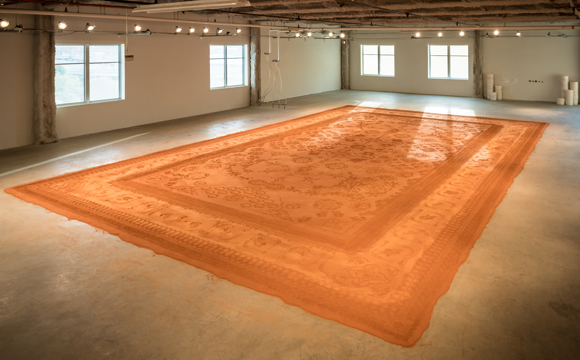 A monumental, low relief sculpture mimicking an intricate patterned rug, made with modified shoe soles imprinting ground & sifted Oklahoma red dirt