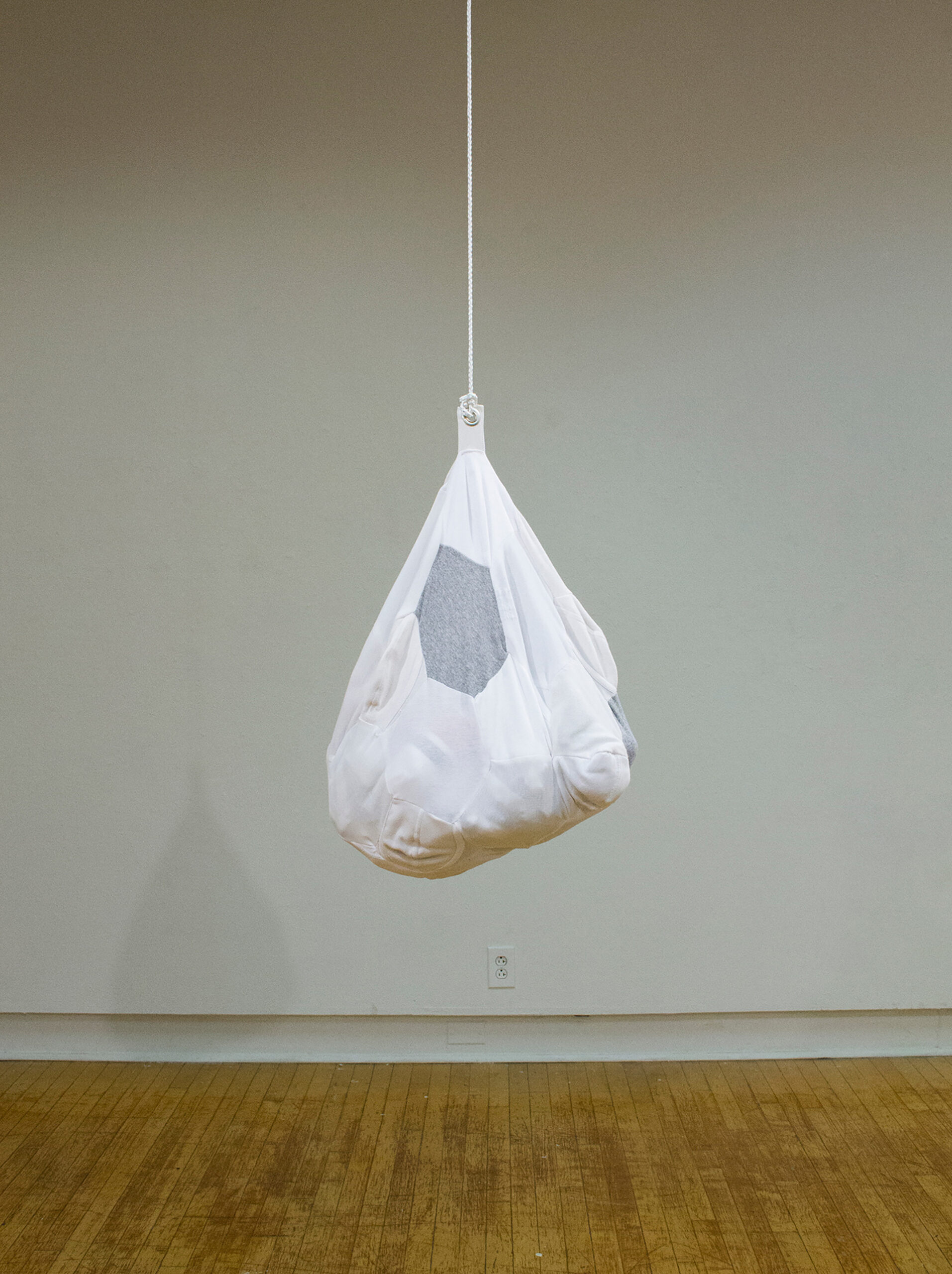 A made from repurposed underwear hangs from a rope, suspended in a gallery space