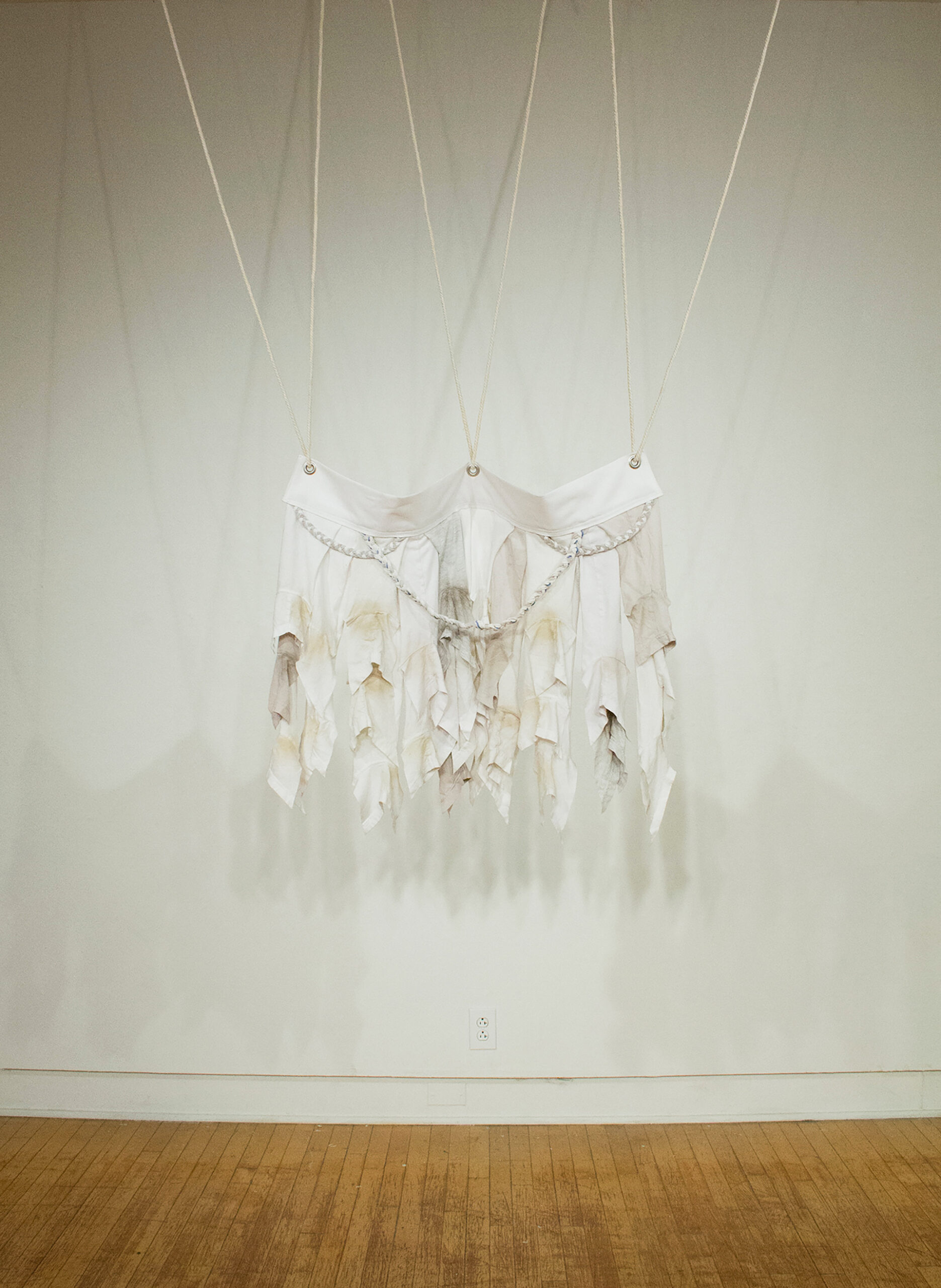 Repurposed undershirts create a non-objective sculpture that hangs from ropes through three grommets