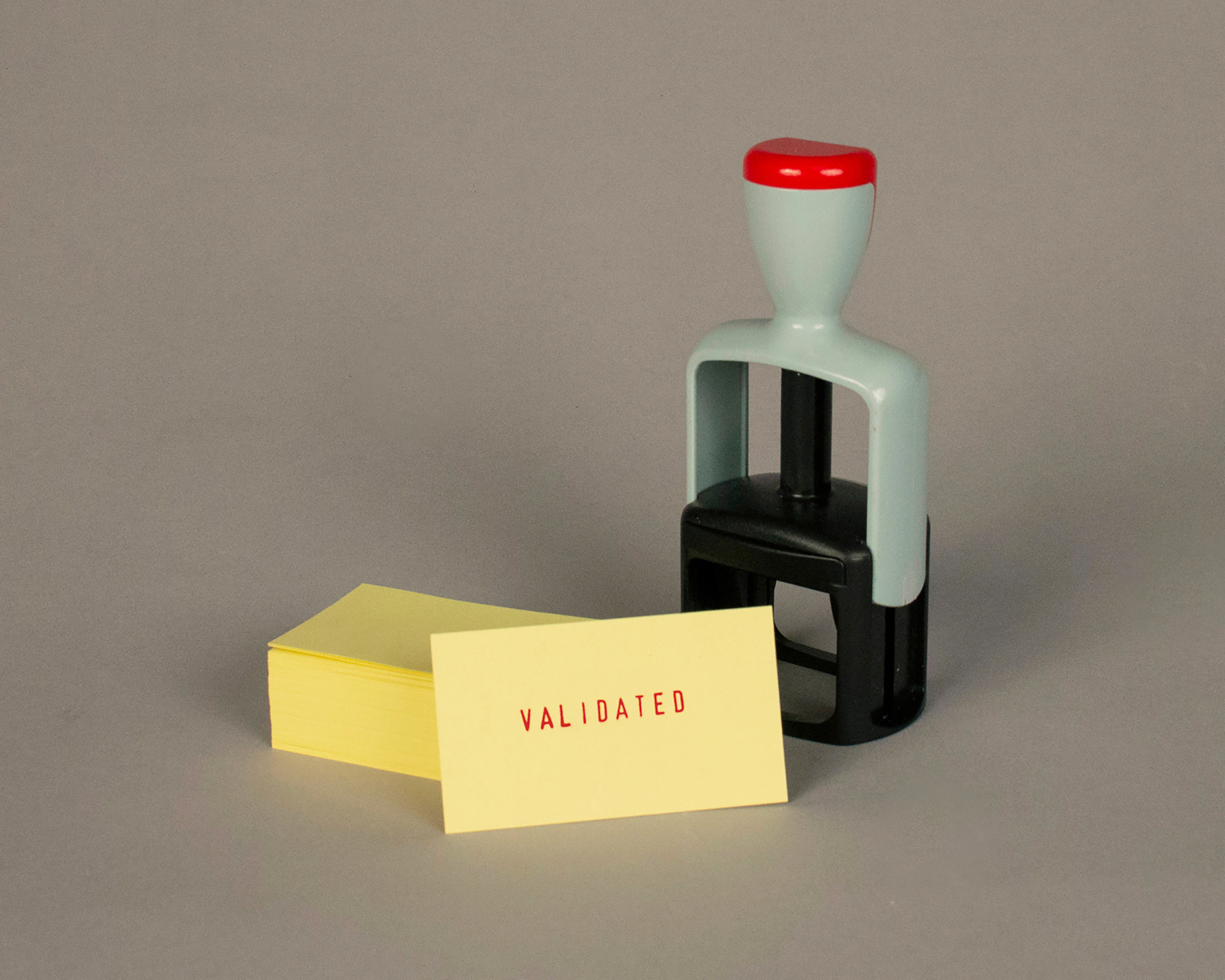A stamper stands next to a stack of business card sized yellow card stock. A single card has the word "validated" printed on it from the stamper.