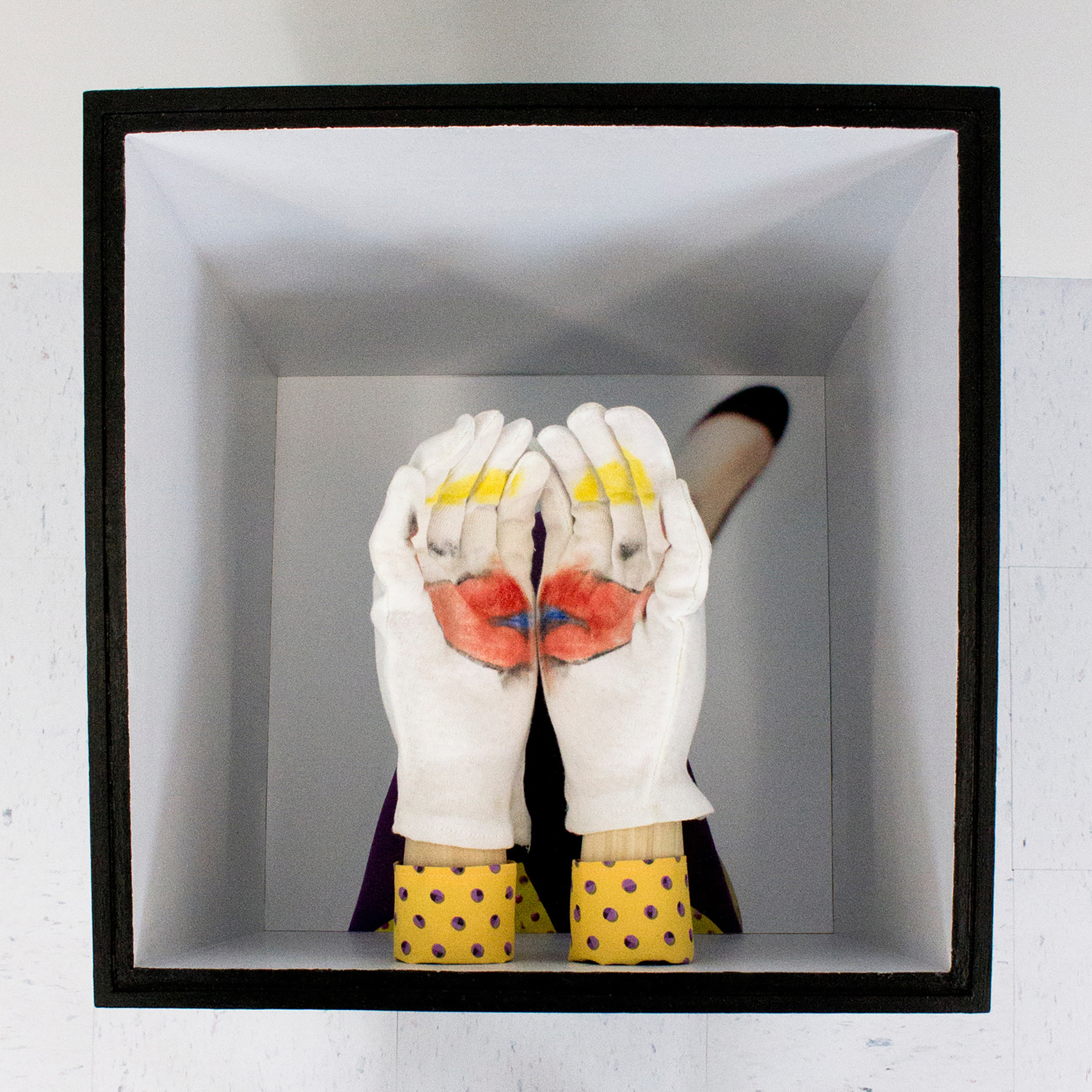 Interior of a box with gloved mannequin hands covered in clown makeup.