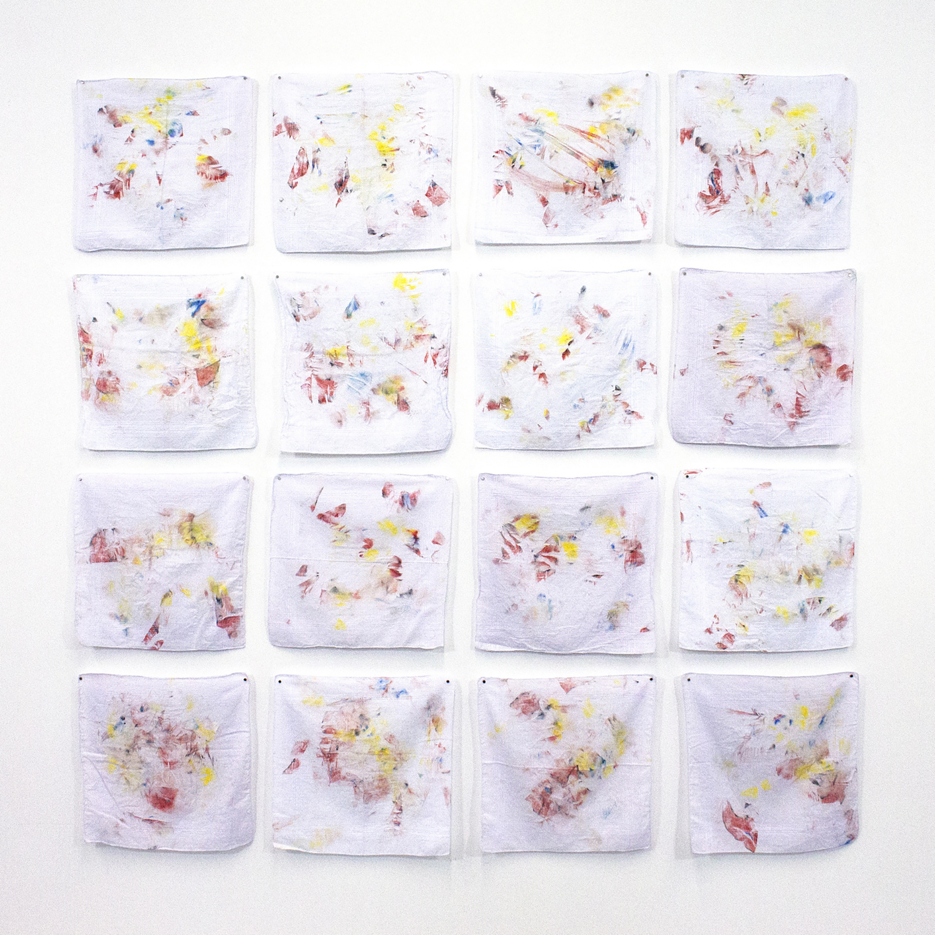 Makeup covered handkerchiefs arranged in a 4x4 grid as impressions from the process of removing the makeup