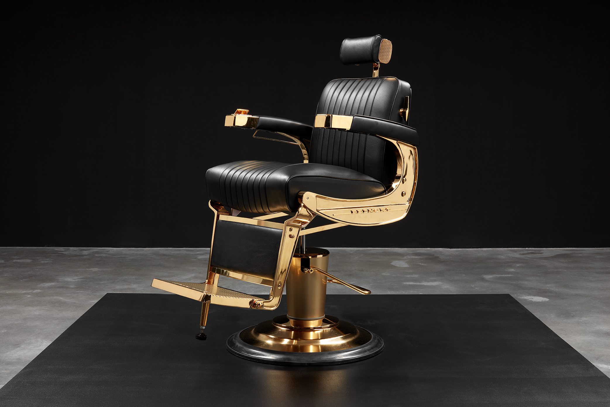 A barber's chair sits in a dark gallery space. The metal work has been gold plated, making it lush, like a throne.