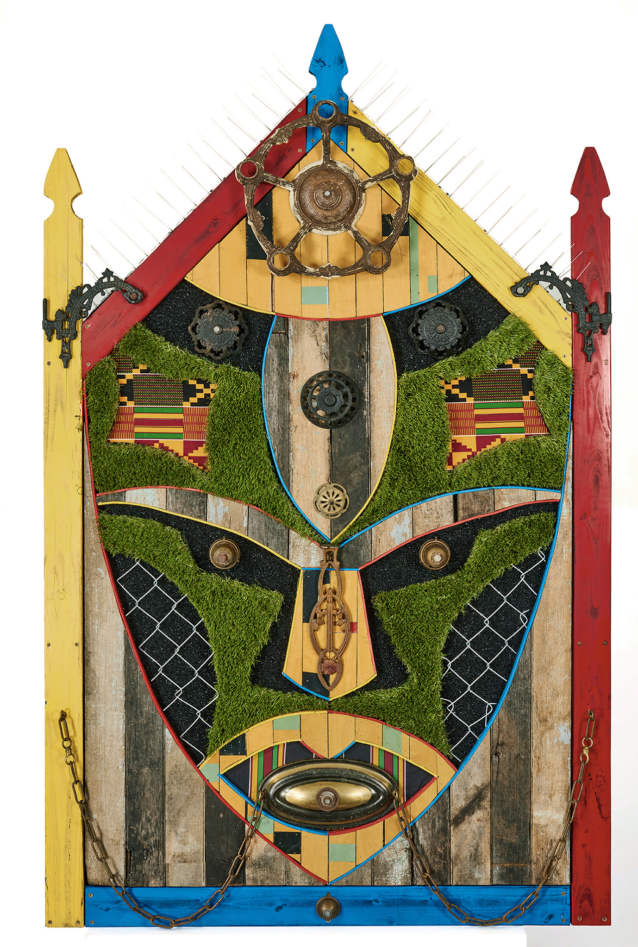 Sentinel, The Defender; by Aaron Coleman. A mixed media assemblage evoking Ghanaian masks, made from fencing, fake turf, and salvaged wood from a neighbor's home lost to gentrification.