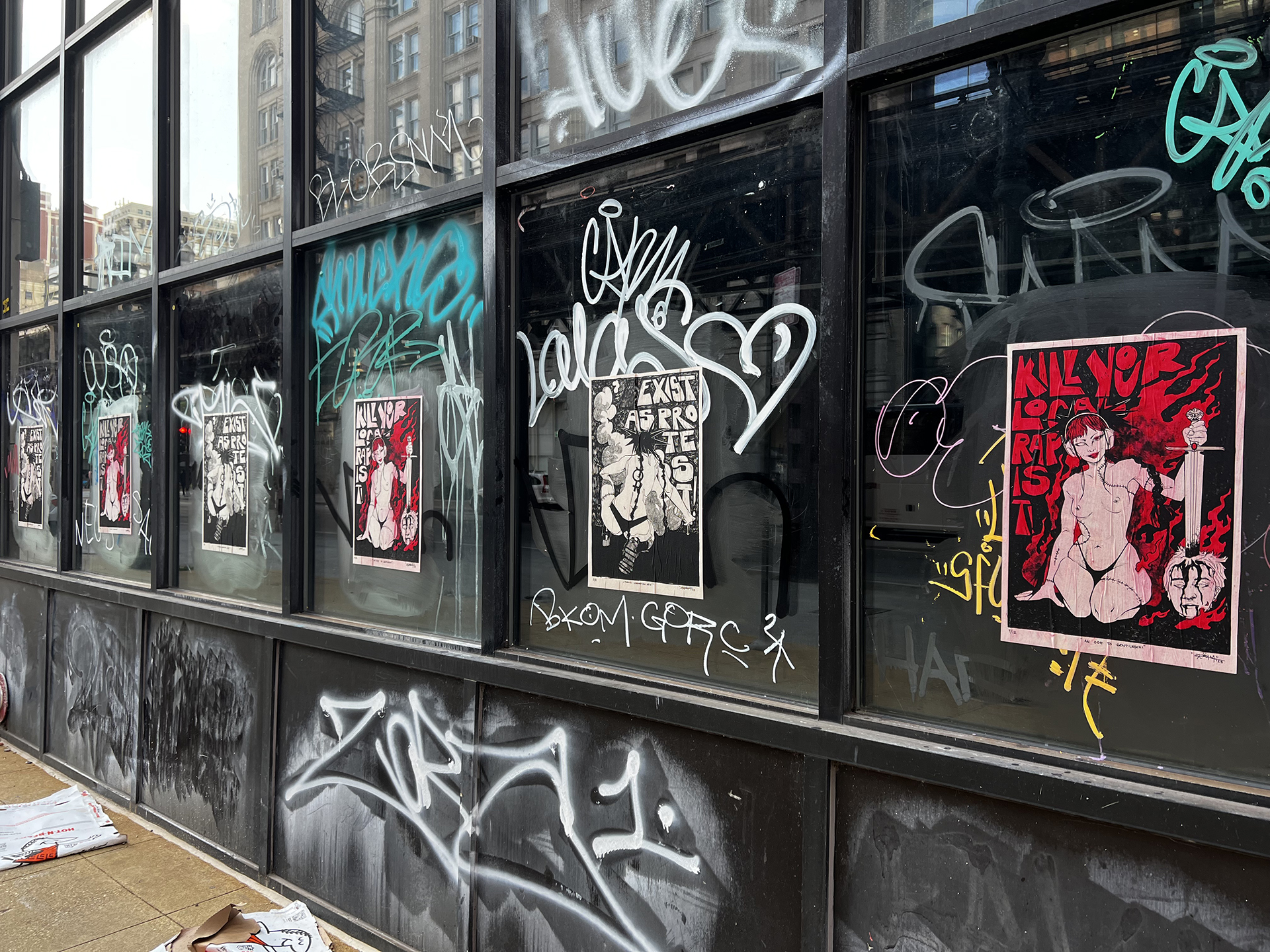 An alternating procession of paste up posters on graffitied windows with the Gentileschi posters alternating with another that says "Exist as protest"