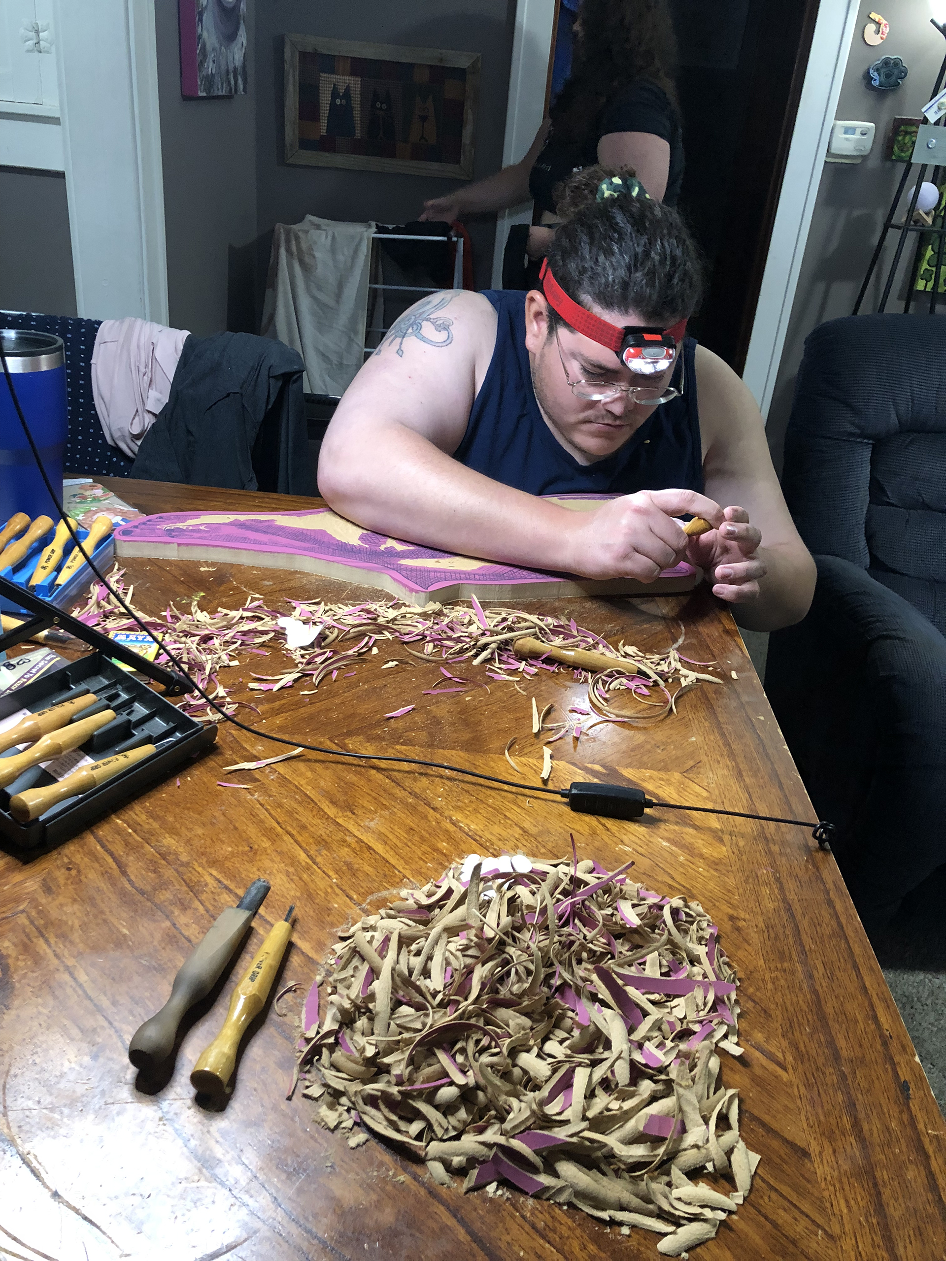 The artist's husband helps carve a block in their home with their partner in the background.