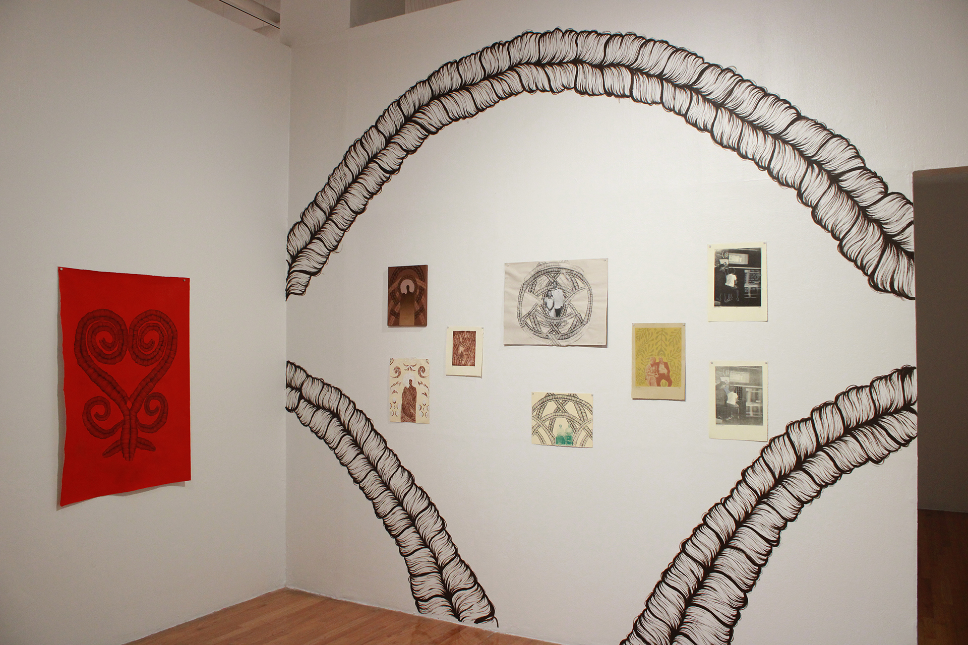 Installation shot of Kai Offet's prints surrounded on the wall with wall-sized arches composed of braids