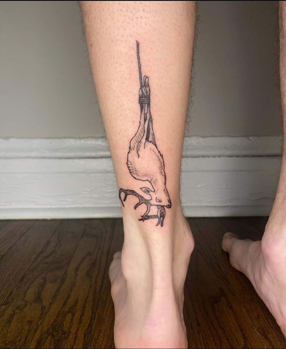 A person's calf tattooed with a deer suspended by its ankles