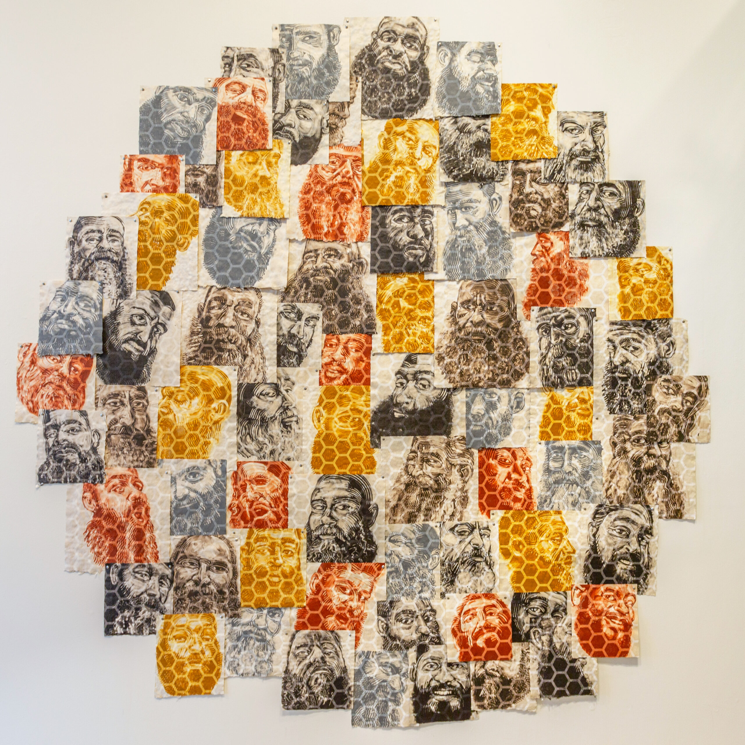 A large circular installation of monoprint portraits of men with prominent beards, printed in yellow, grey, brown, and red. A large hexagonal pattern is in every portrait, making the installation appear as if it is an enormous honeycomb.