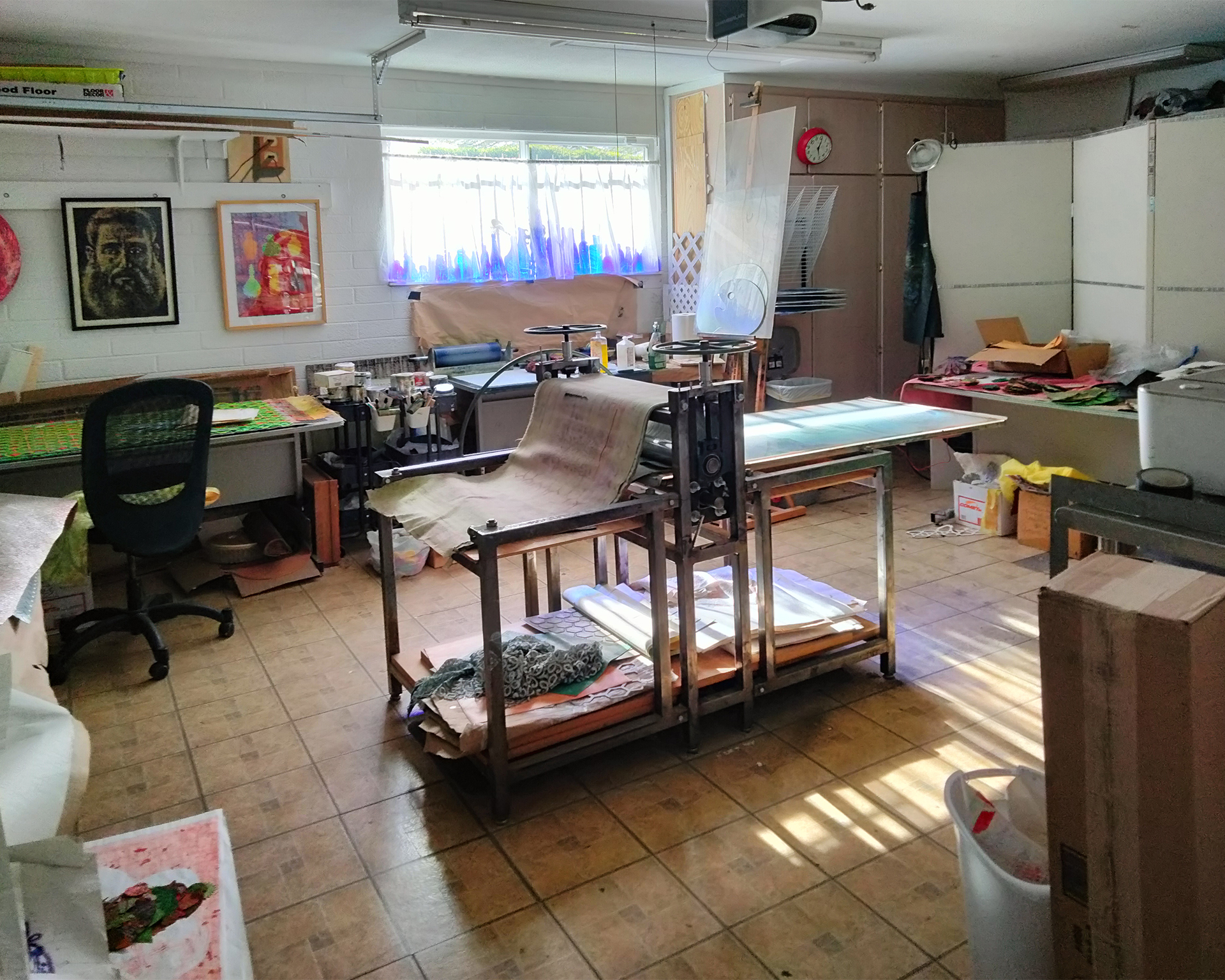 Photo of he artist's studio including an etching press and prints on the wall.