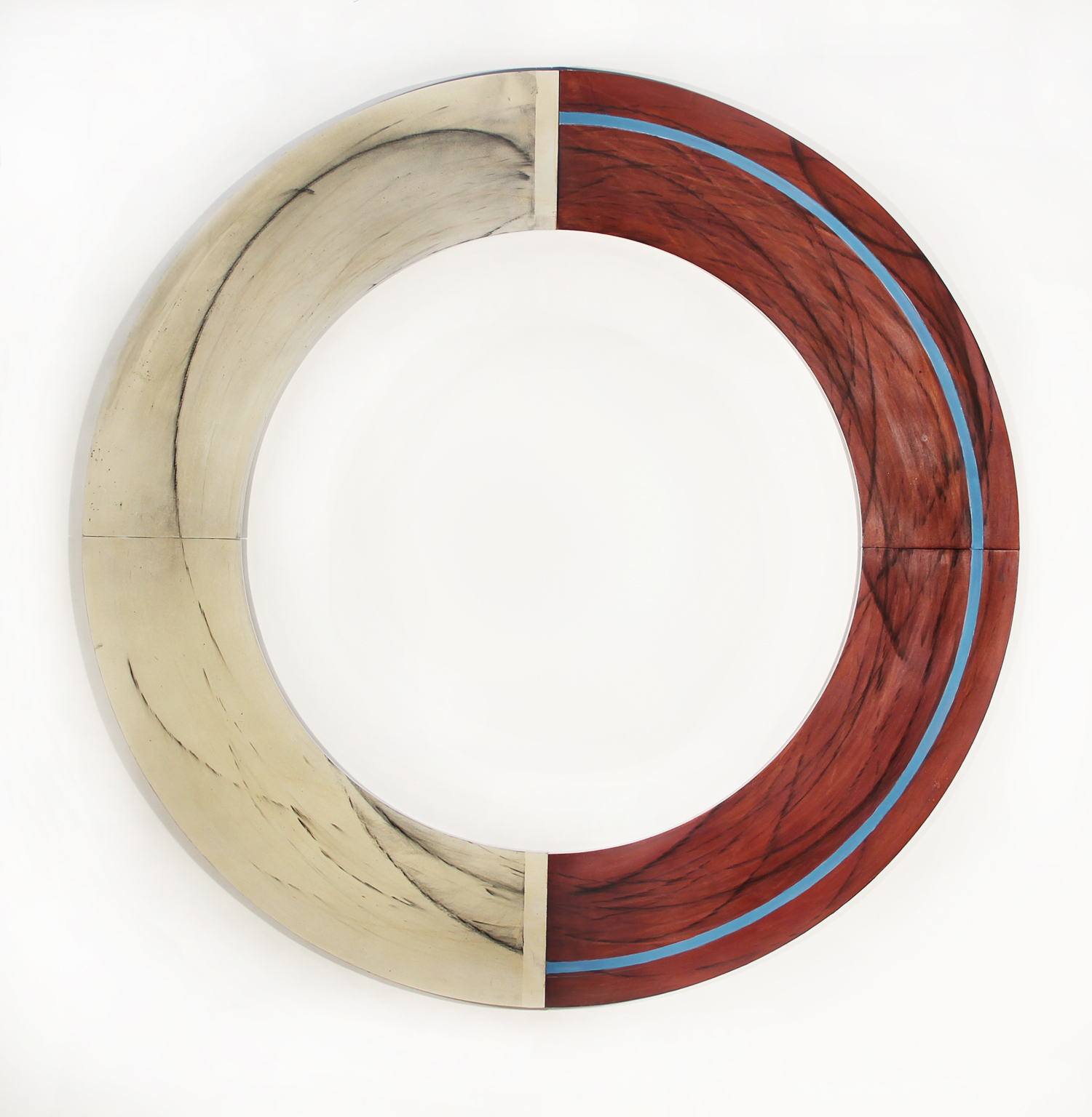 A ring of bisected wood, light on the left, stained red maple with a thin line of blue on the left. Atop are calligraphic marks in charcoal created by the artist passing a charcoal covered rope over the piece leaving the evidence of the trick roping on the sculpture.