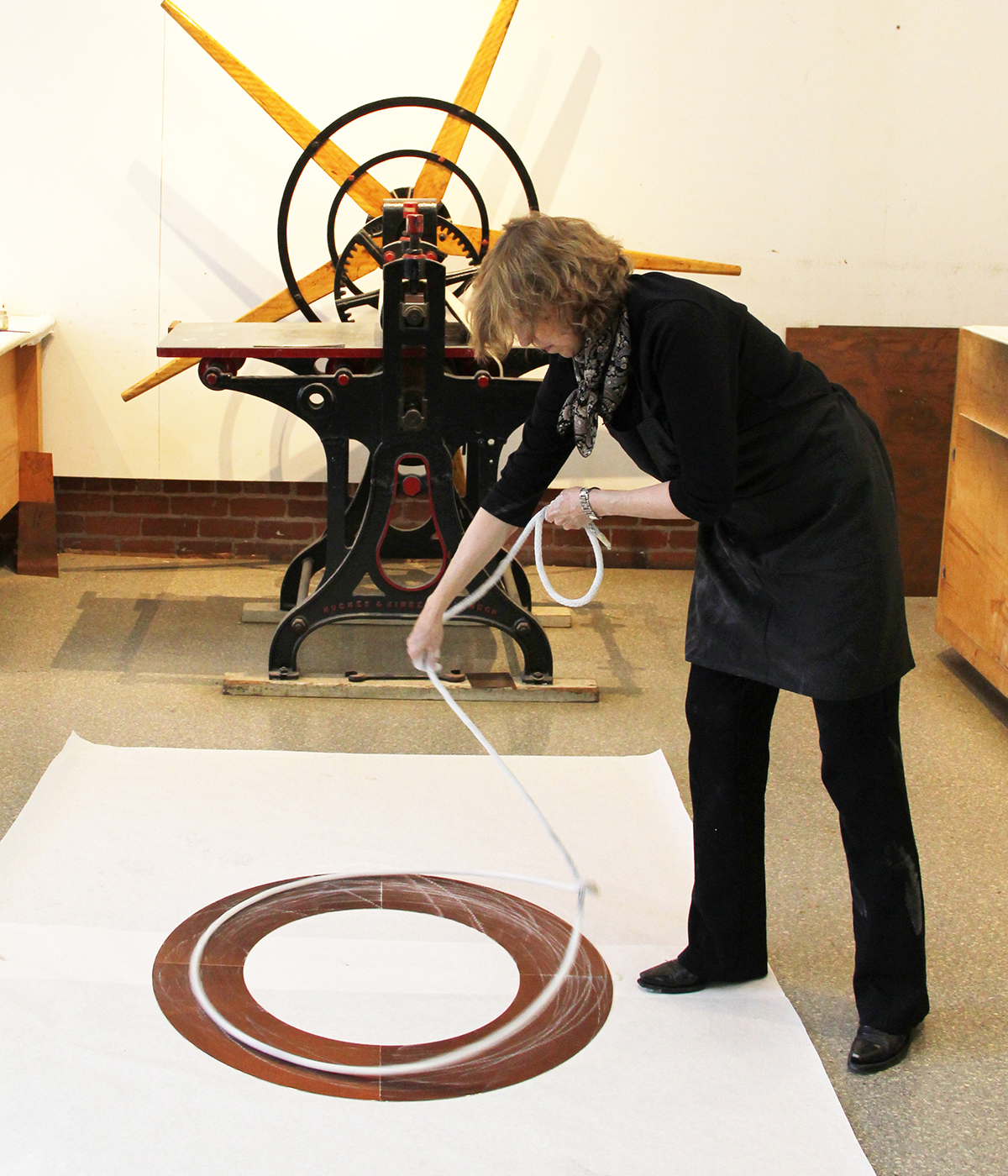 The artist stands over a brown ring, spinning a chalk covered lasso, leaving impressions of the spinning rope on the brown ring, using the lasso as a drawing tool, documenting the motion.