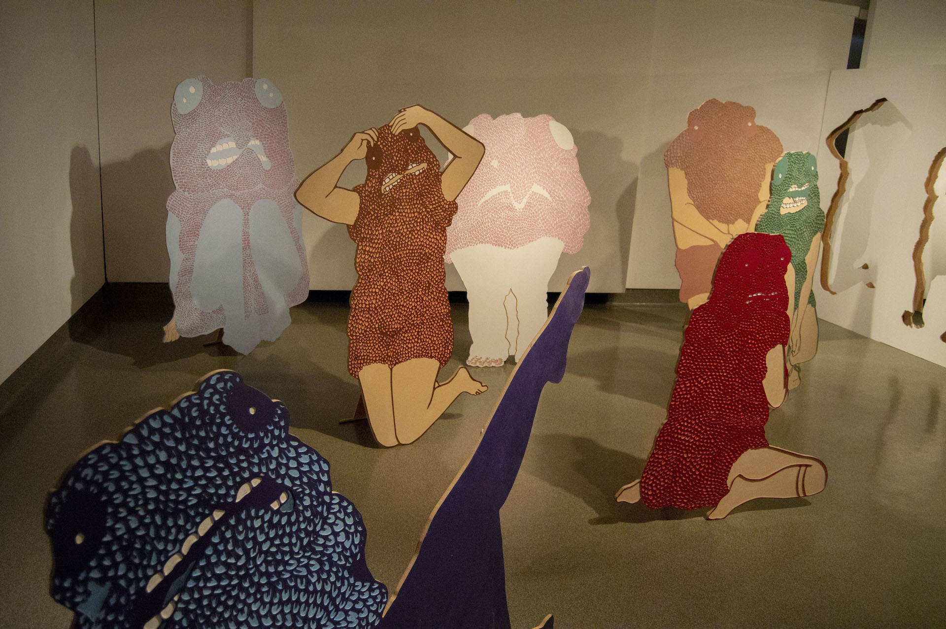 Several free-standing near human-scale monstrous figures covered in colorful scales populate a gallery space.