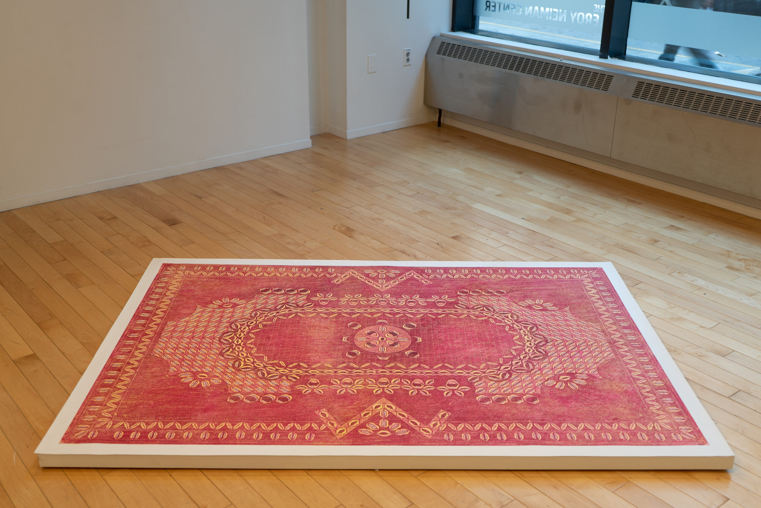 A woodcut of a large red rug sits on a plywood platform. The rug is composed of mouths in various positions and scales to create an elaborate pattern.