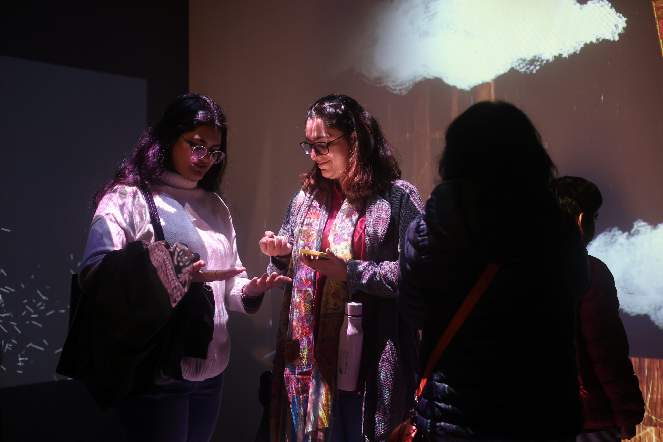 Viewers stand before the Mera Kamra animation of clouds flooding a room. Their bodies are covered in projections from the artist's other works.