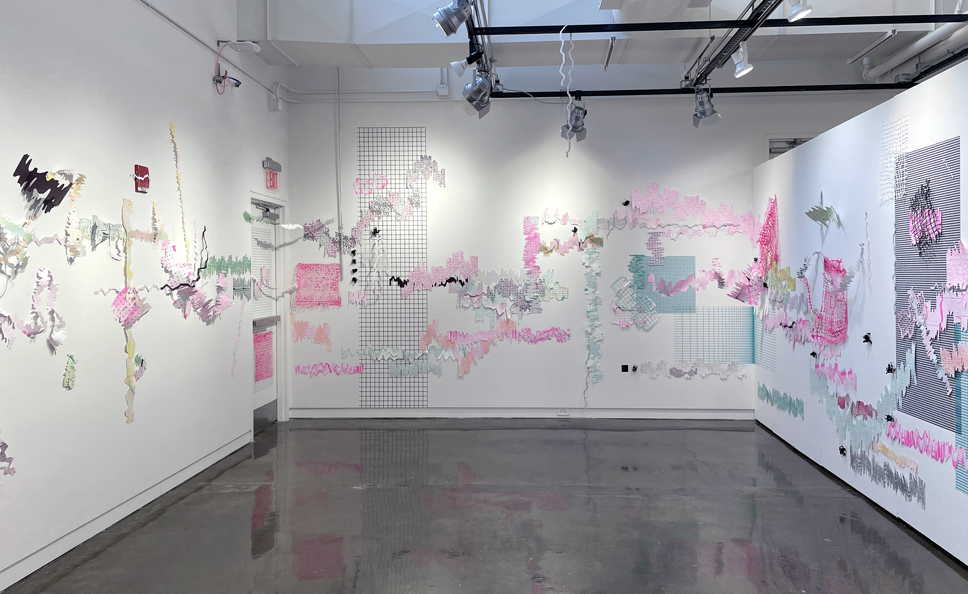 Photograph of a room with three white walls. An interactive paper, vinyl and handmade paper installation is on the walls. The paper prints are bright pink, teal, yellow and orange, placed on top of teal and black vinyl grids.