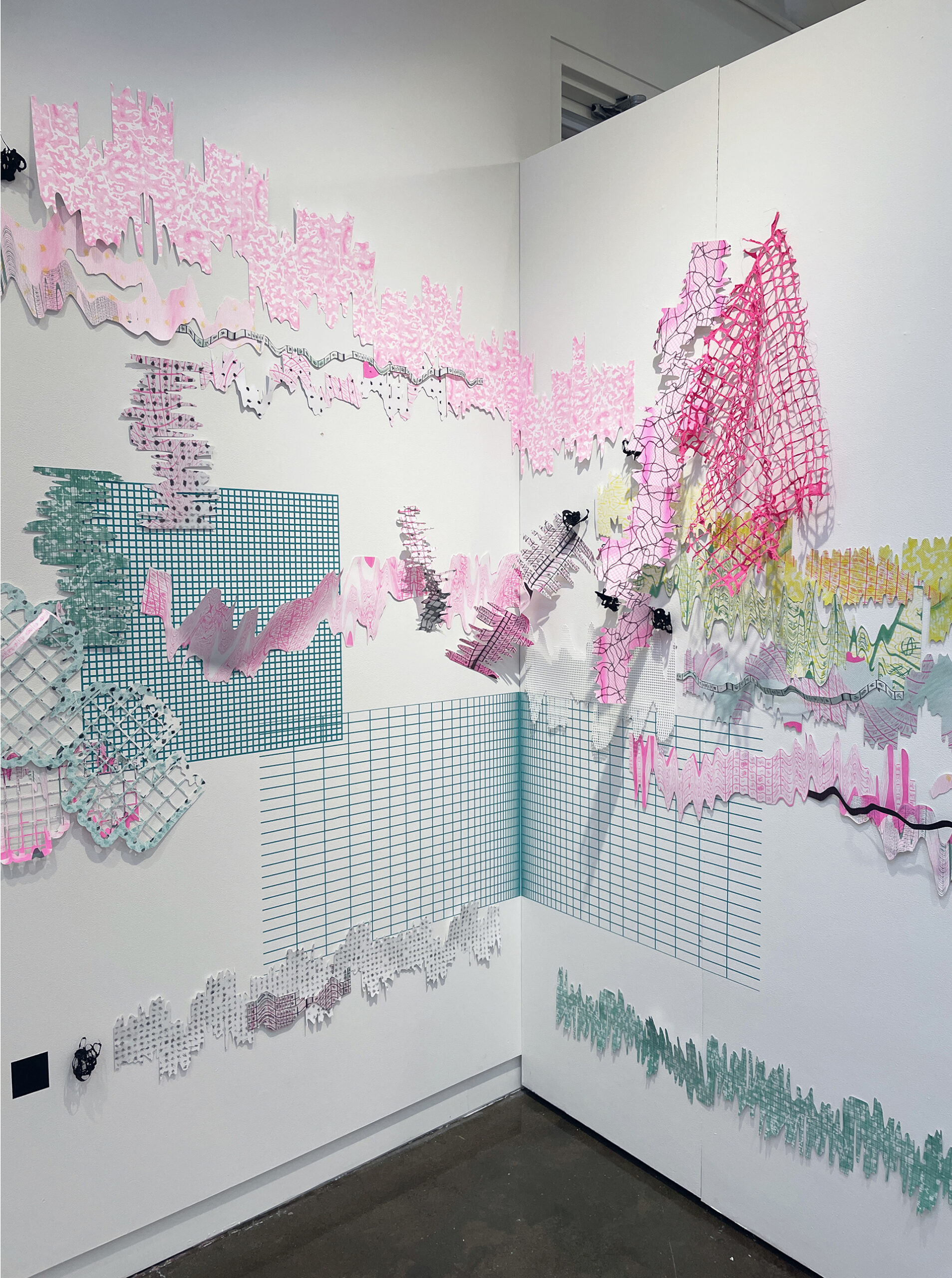 A photo of two walls meeting in a corner. There are two teal colored vinyl grids on the walls, one of which meets in the corner of the walls and branches out. There are cut paper prints and handmade paper grids hung on the wall, interacting with one another.