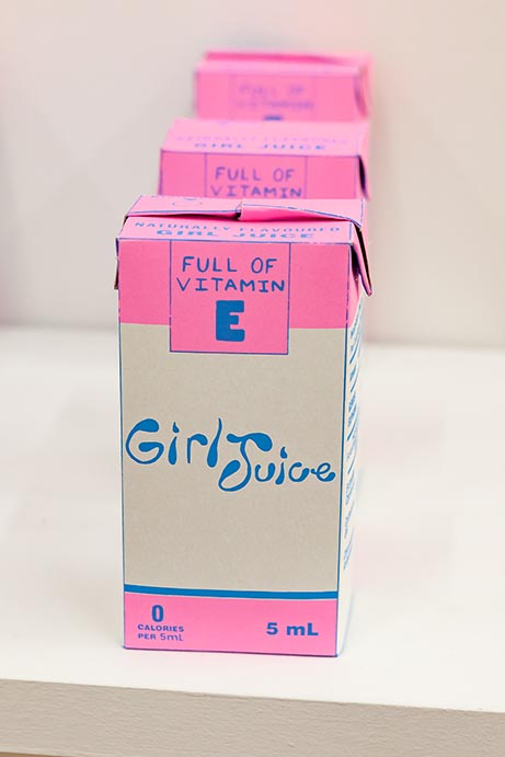 A column of paper cartons of "Girl Juice", an alternative to typical hormone therapy, printed in a pink motif.