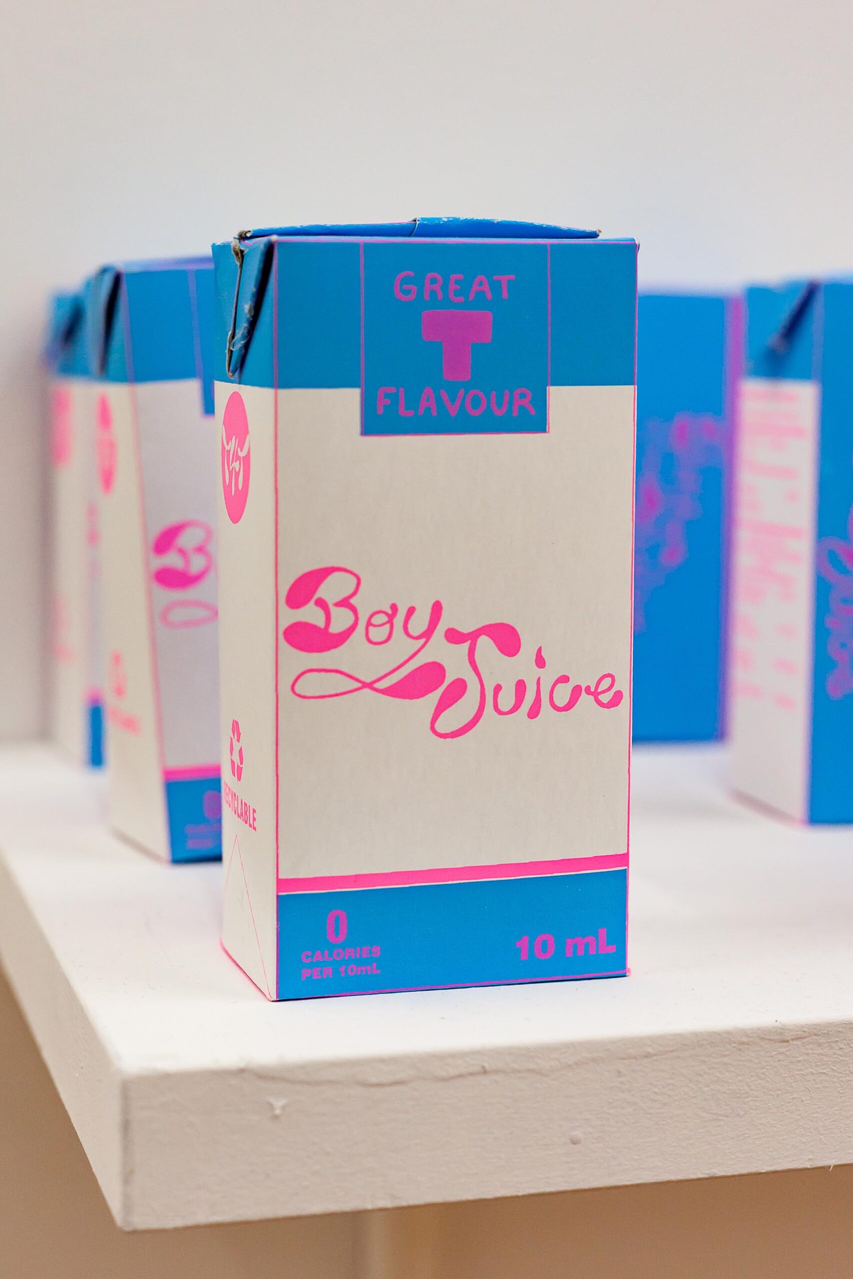 A column of paper cartons of "Boy Juice", an alternative to typical hormone therapy, printed in a blue motif.