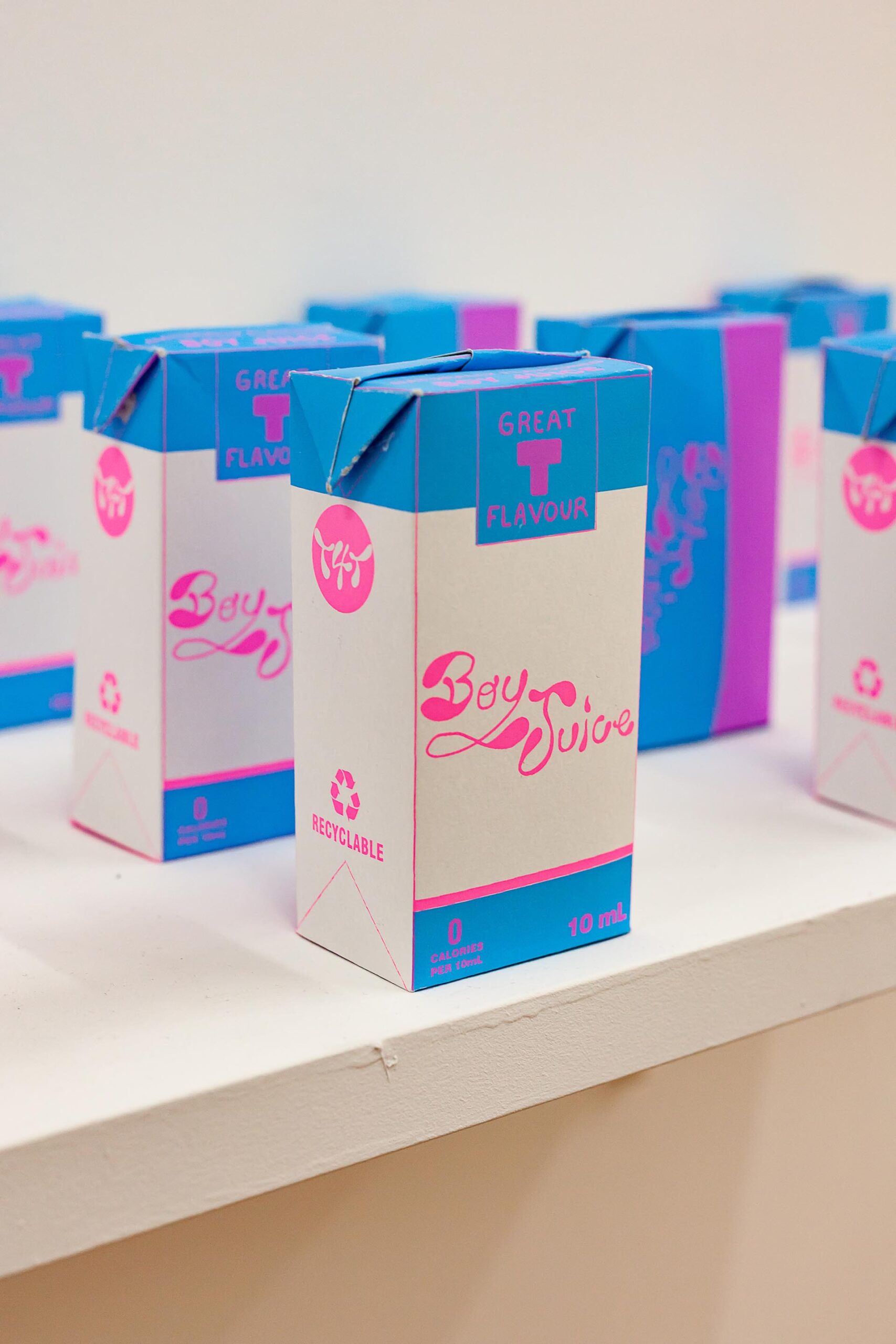 A column of paper cartons of "Boy Juice", an alternative to typical hormone therapy, printed in a blue motif.