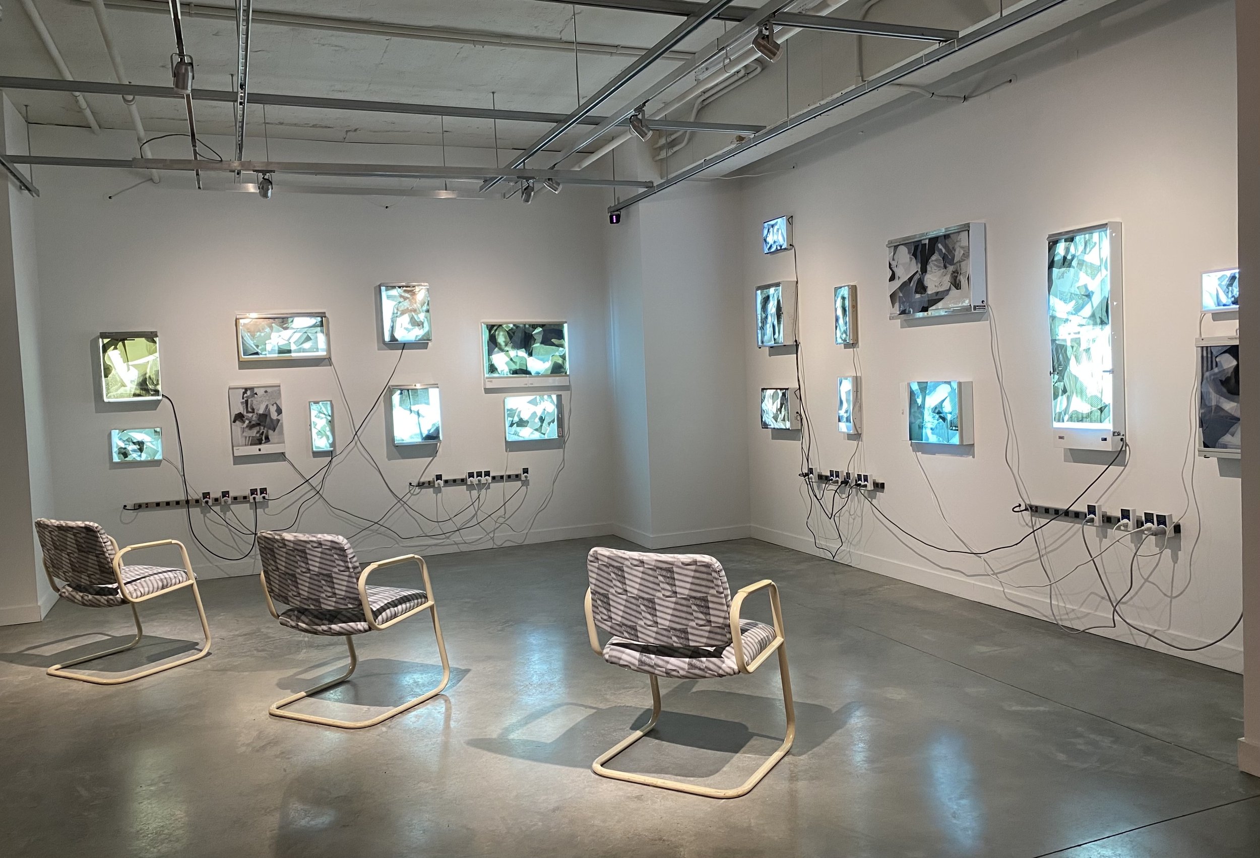 Nineteen X-ray boxes hang on the wall illuminating layers of printed transparency. Boxes turn on and off connected to dangling wires plugged into timers. Three reupholstered waiting room chairs are arranged in a diagonal line in front of the X-Ray Boxes offering the viewers a seat.