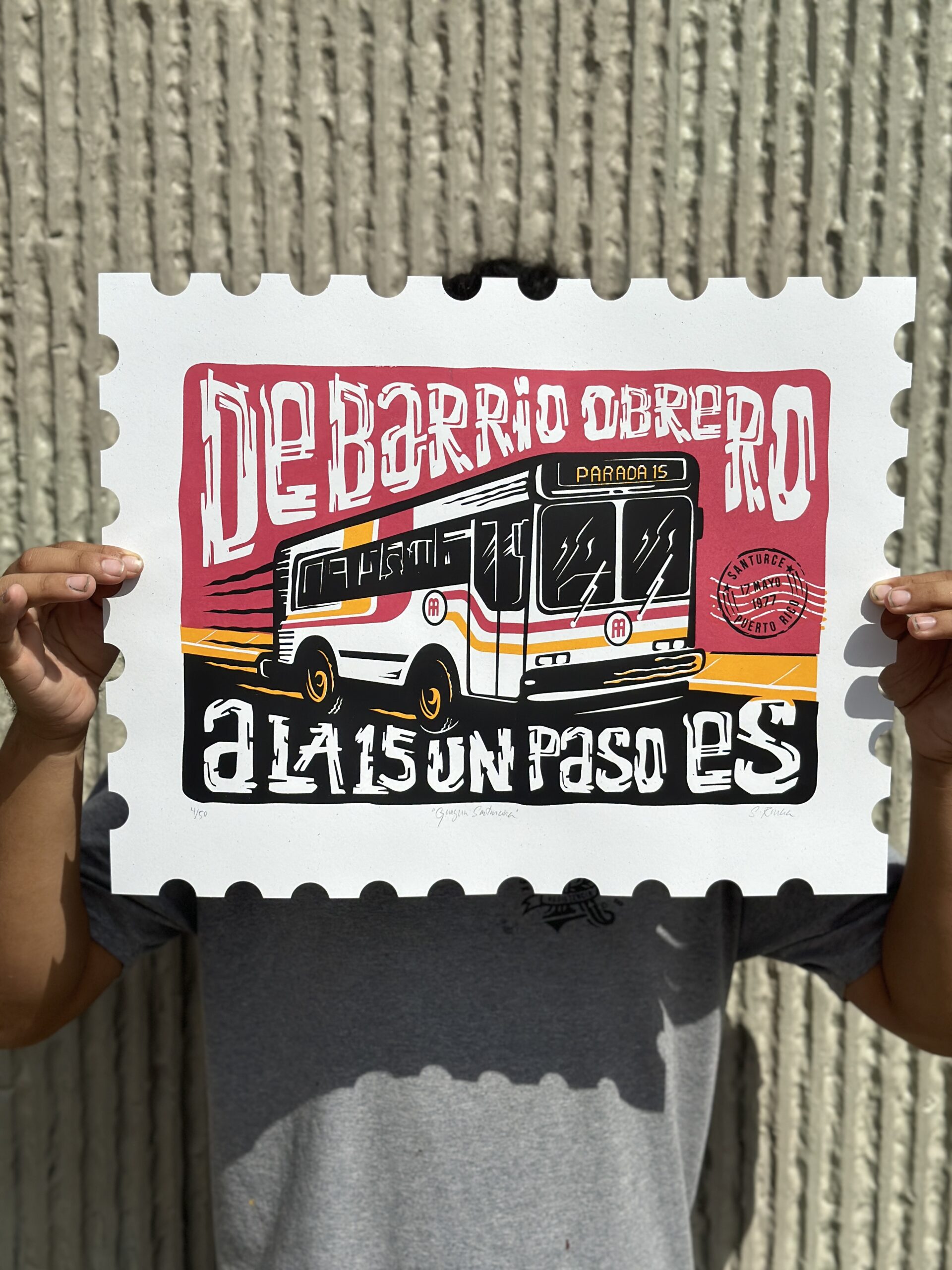 The artist holds the print of a bus with the edges of the paper scalloped like a postage stamp
