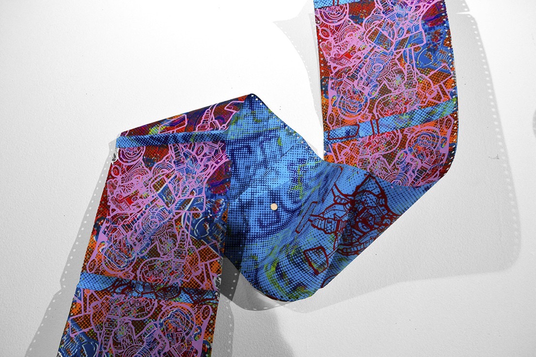 An installation of dot matrix printer paper folded upon itself on the wall and floor covered in a dense application of screenprinted robotic imagery in linework and textures