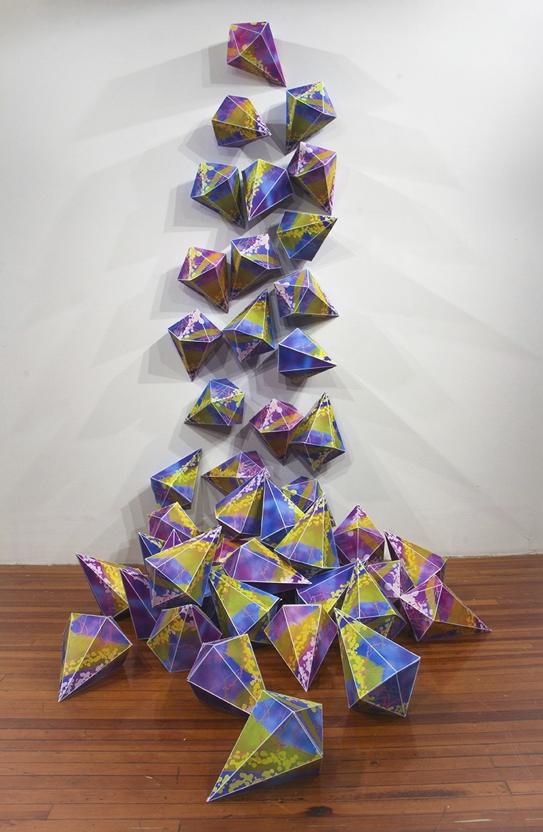 Dozens of gem shaped, screenprinted paper forms cascade down the gallery wall and onto the floor
