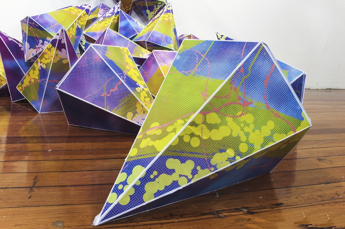 Dozens of gem shaped, screenprinted paper forms cascade down the gallery wall and onto the floor